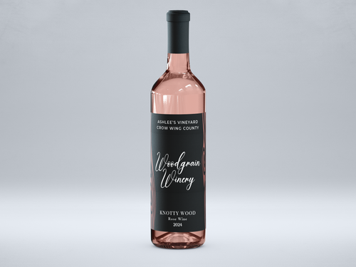 This is a picture of woodgrain winerys Rose wine named Wildwood. The bottle is standing vertically and has a black label with rose gold metal flake woodgrain. The words on the label are white. The image views the bottle from the front.