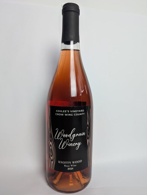 This is a picture of woodgrain winerys Rose wine named Wildwood. The bottle is standing vertically and has a black label with rose gold metal flake woodgrain. The words on the label are white. The image views the bottle from the front.